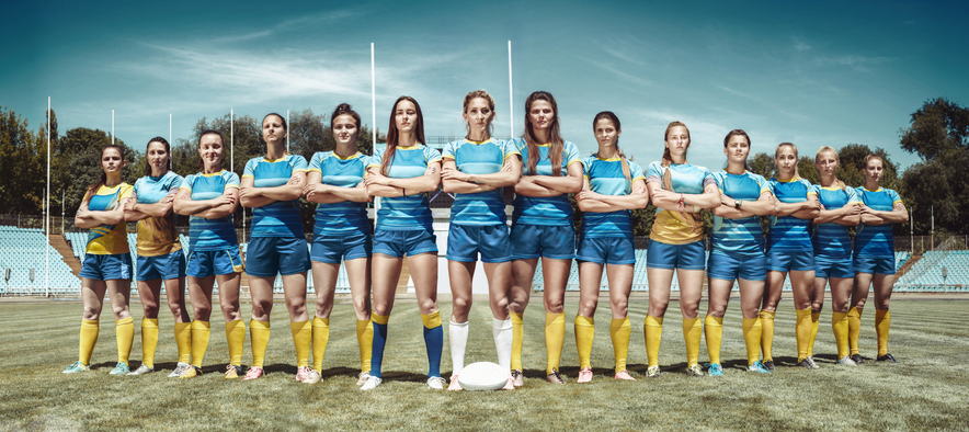 Strength and beauty. Female team of rugby players standing crossing hand at the field in sunny day. Fit caucasian models as a professional sportswoman. Sport competition, motion, movement, fight.